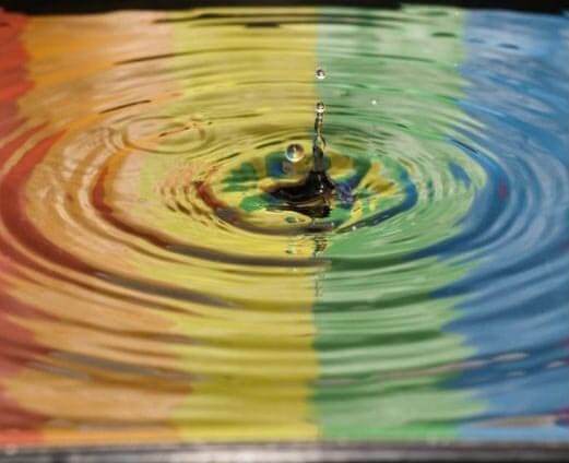 photo of a water drop creating ripples with a reflection of a rainbow flag